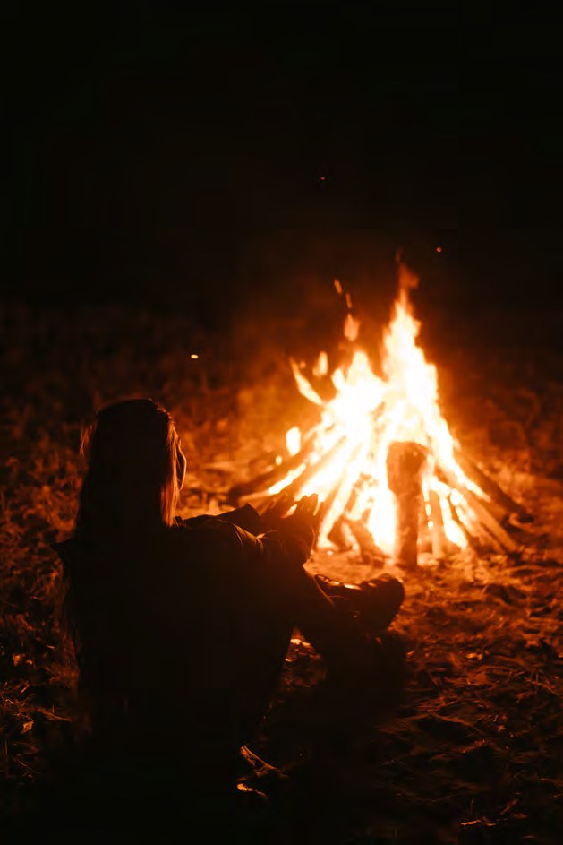 Kampvuur in het donker, met iemand die er warm bij zit