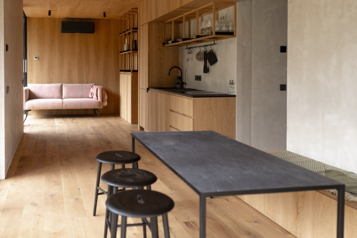 De woonruimte van een eco lodge: de zwarte eettafel met krukken, daarachter de keuken en de roze bank