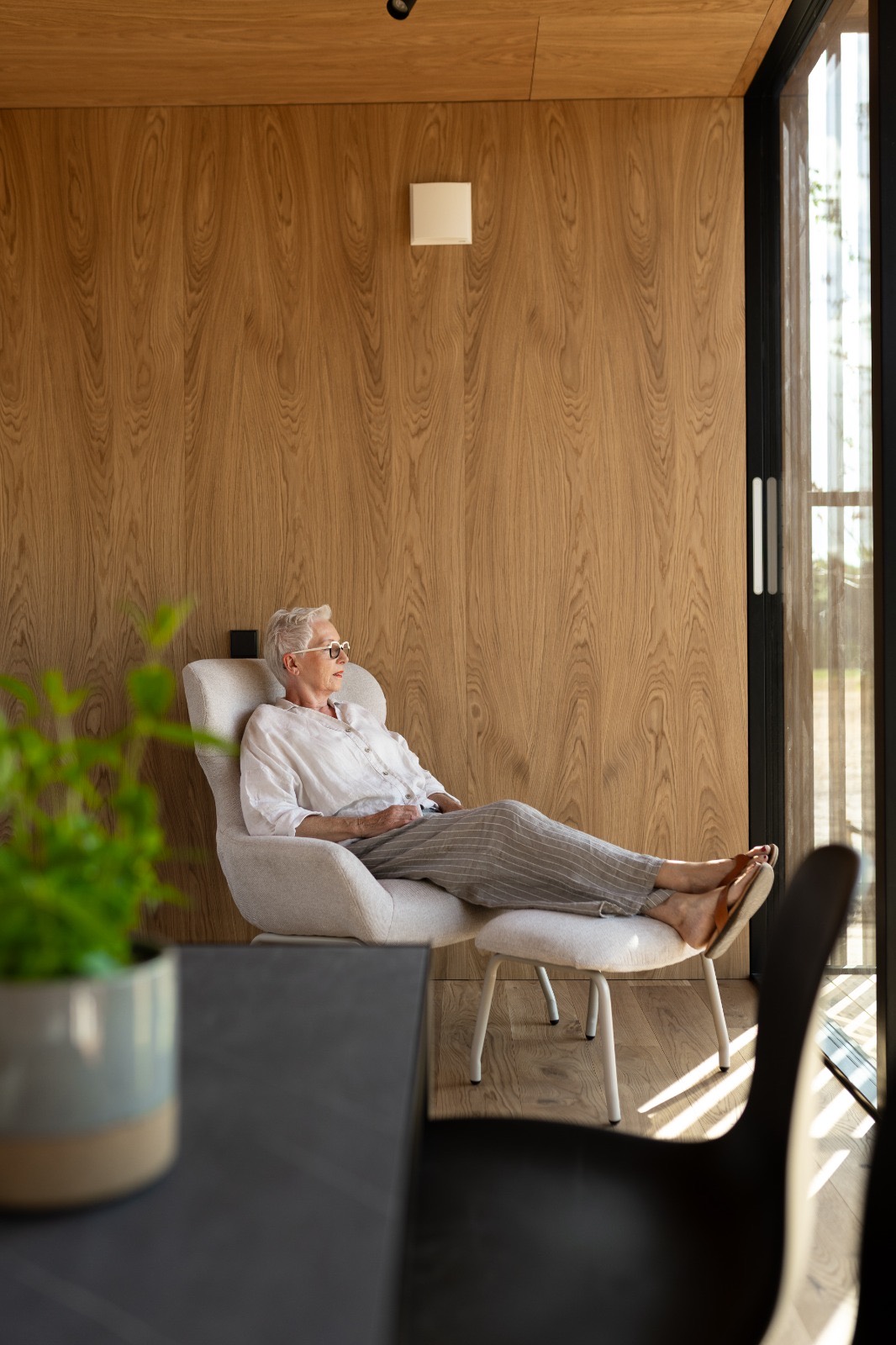 Relaxstoel met voetenbankje voor het raam, met het natuurlandschap erachter